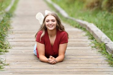 Young woman lying on a wooden path smiling at the camera.