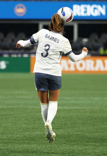 Female soccer player Barnes heading the ball during a match.