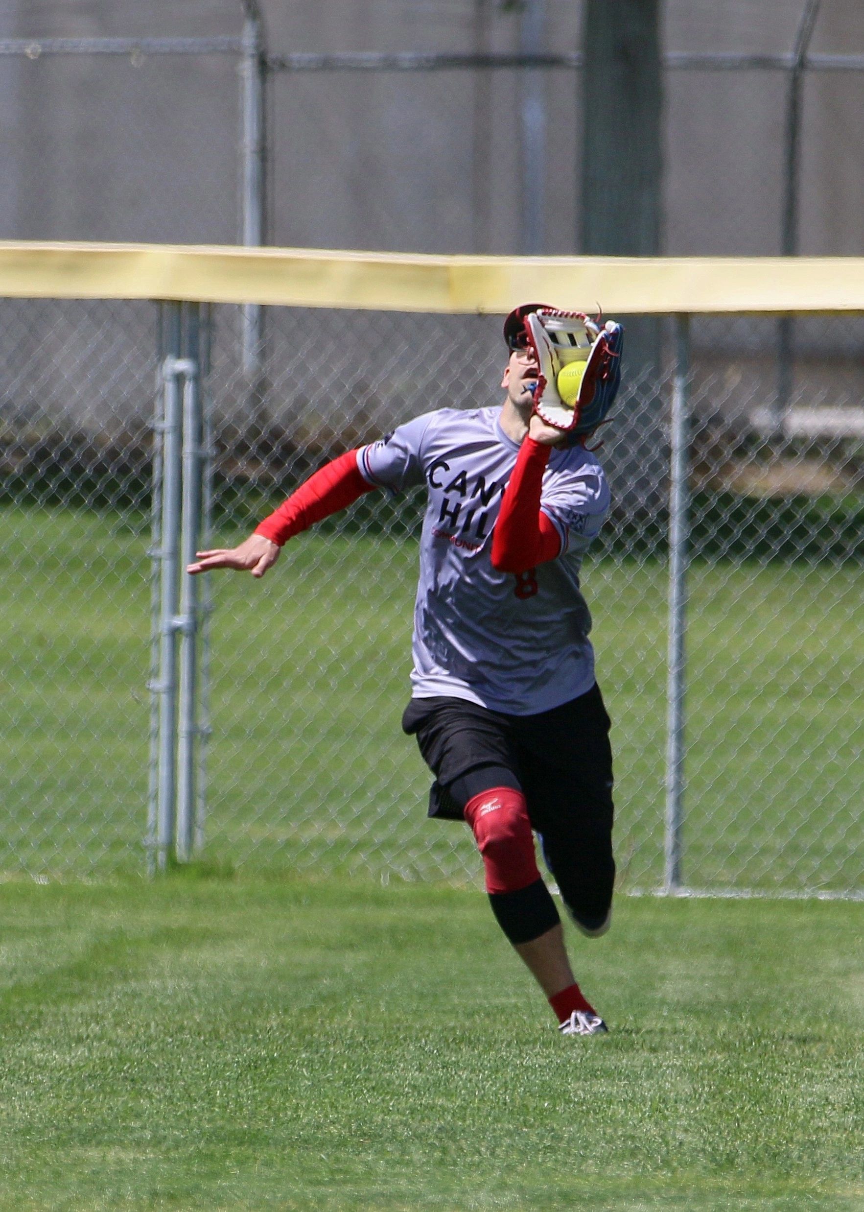 Softball player catching a ball with glove in the outfield.
