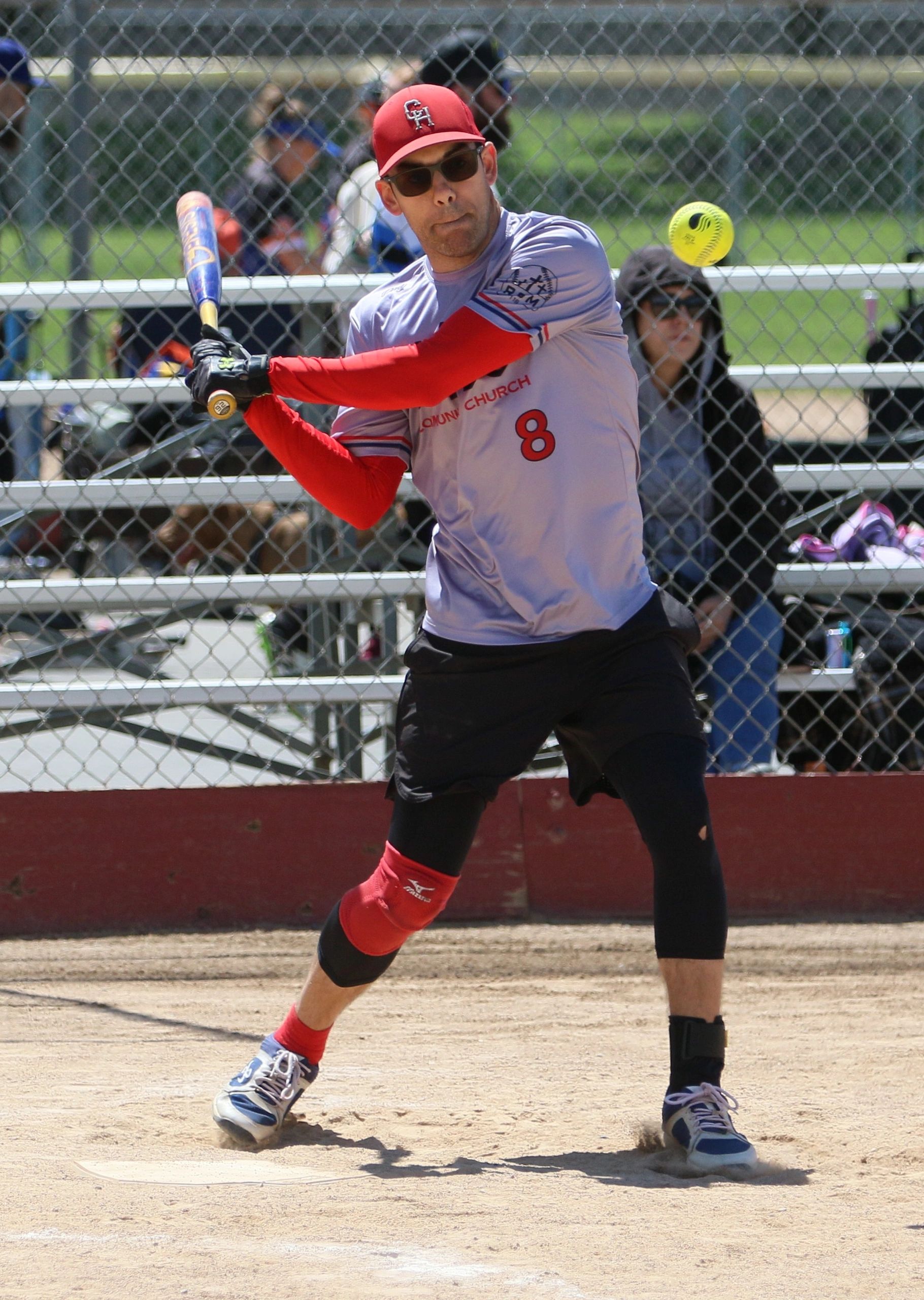 Man in red cap preparing to hit a softball during a game.