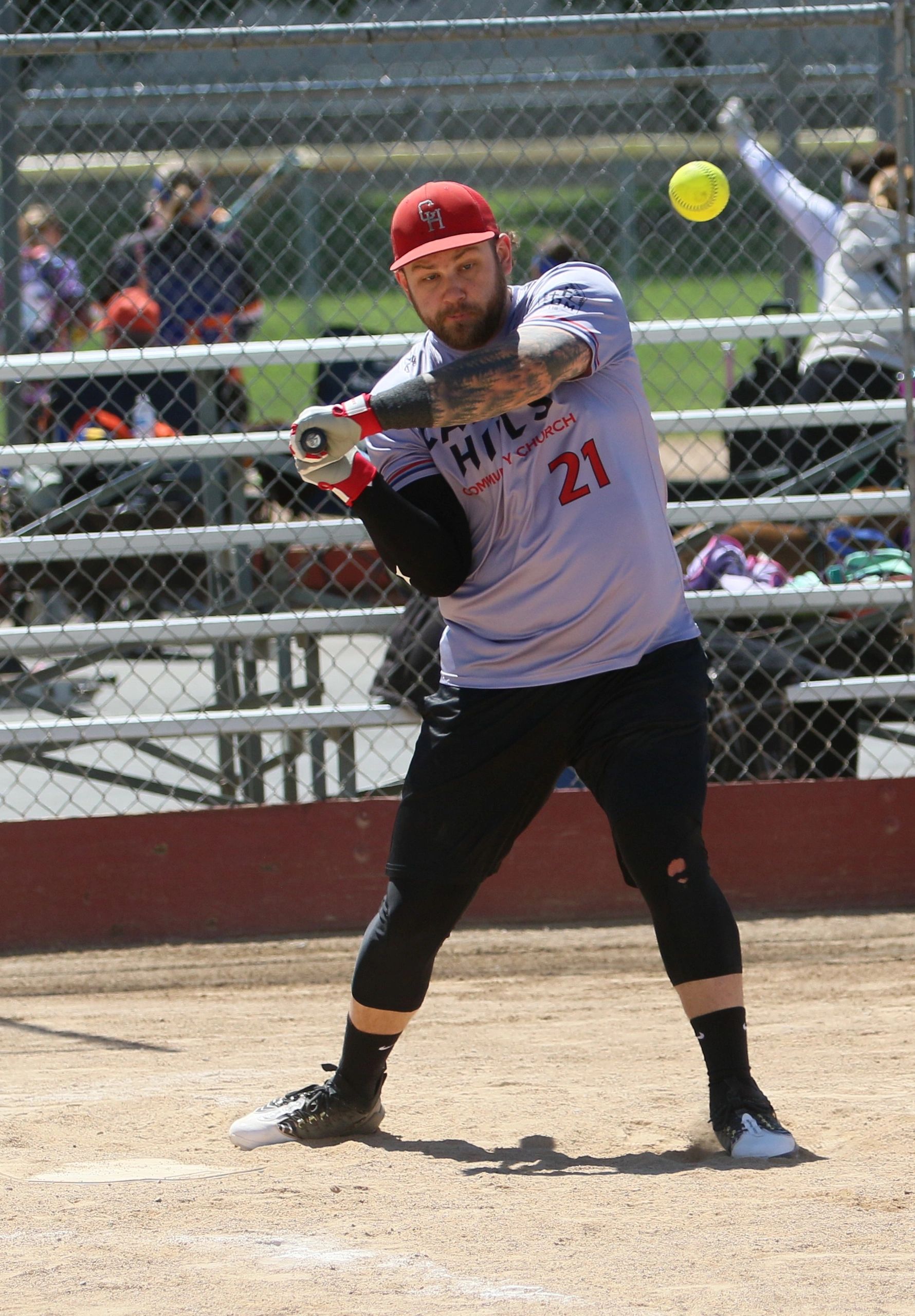 Softball player in mid-swing hitting a yellow ball during a game.