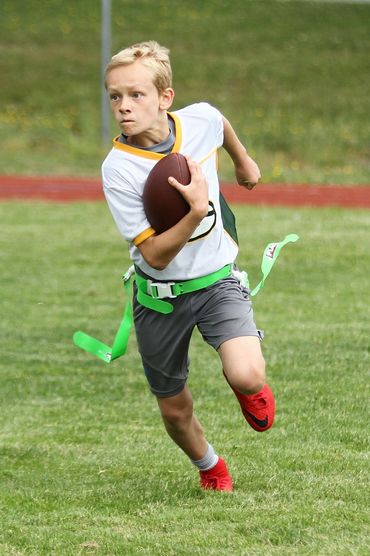 A young boy runs with a football in a flag football game.