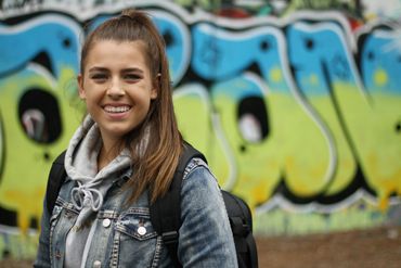 Young woman with a backpack smiling in front of graffiti.