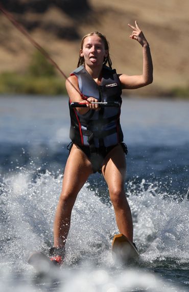 Young woman water skiing, making a playful hand gesture.