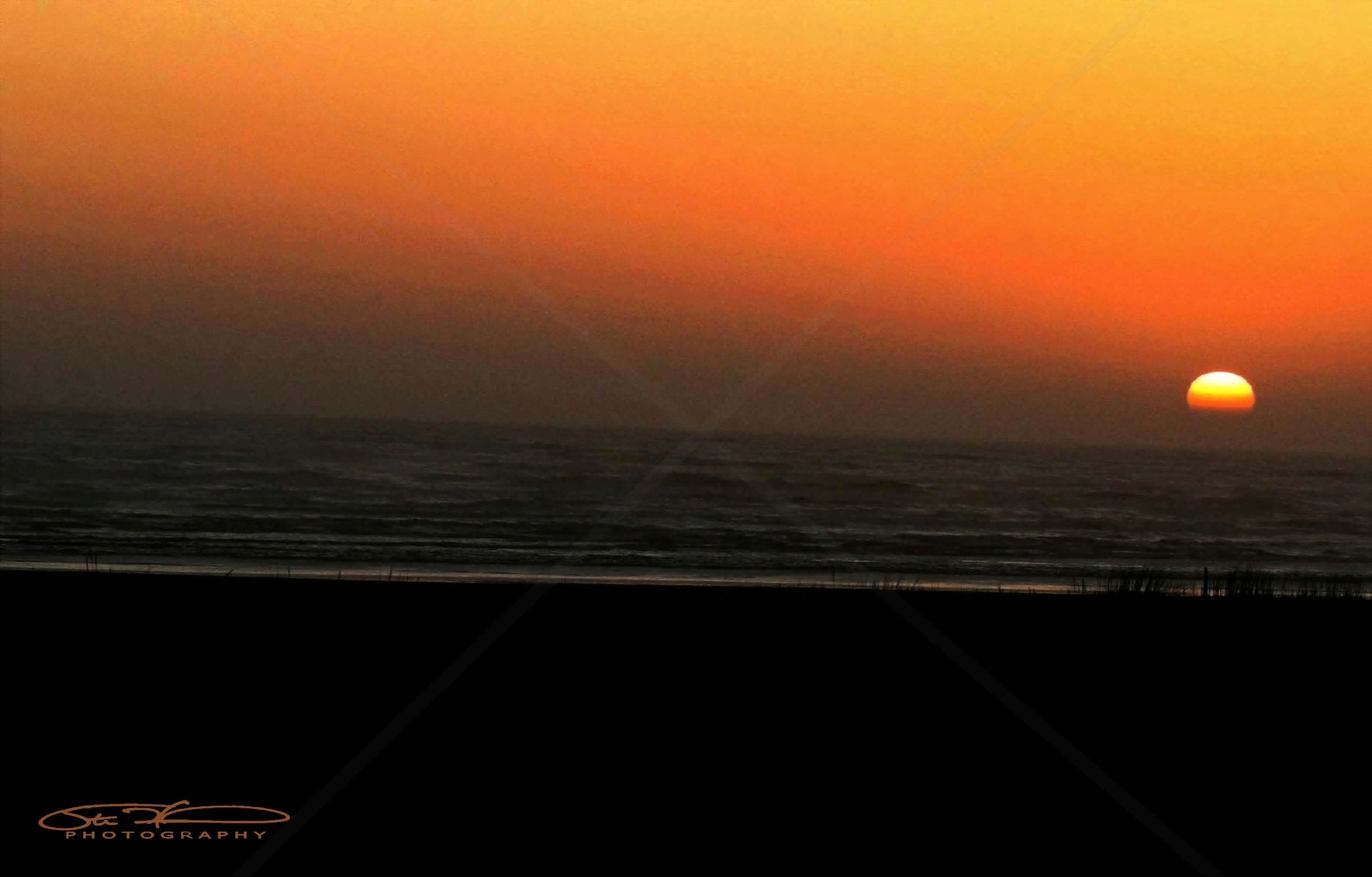 Sun setting over the ocean with a gradient orange sky.