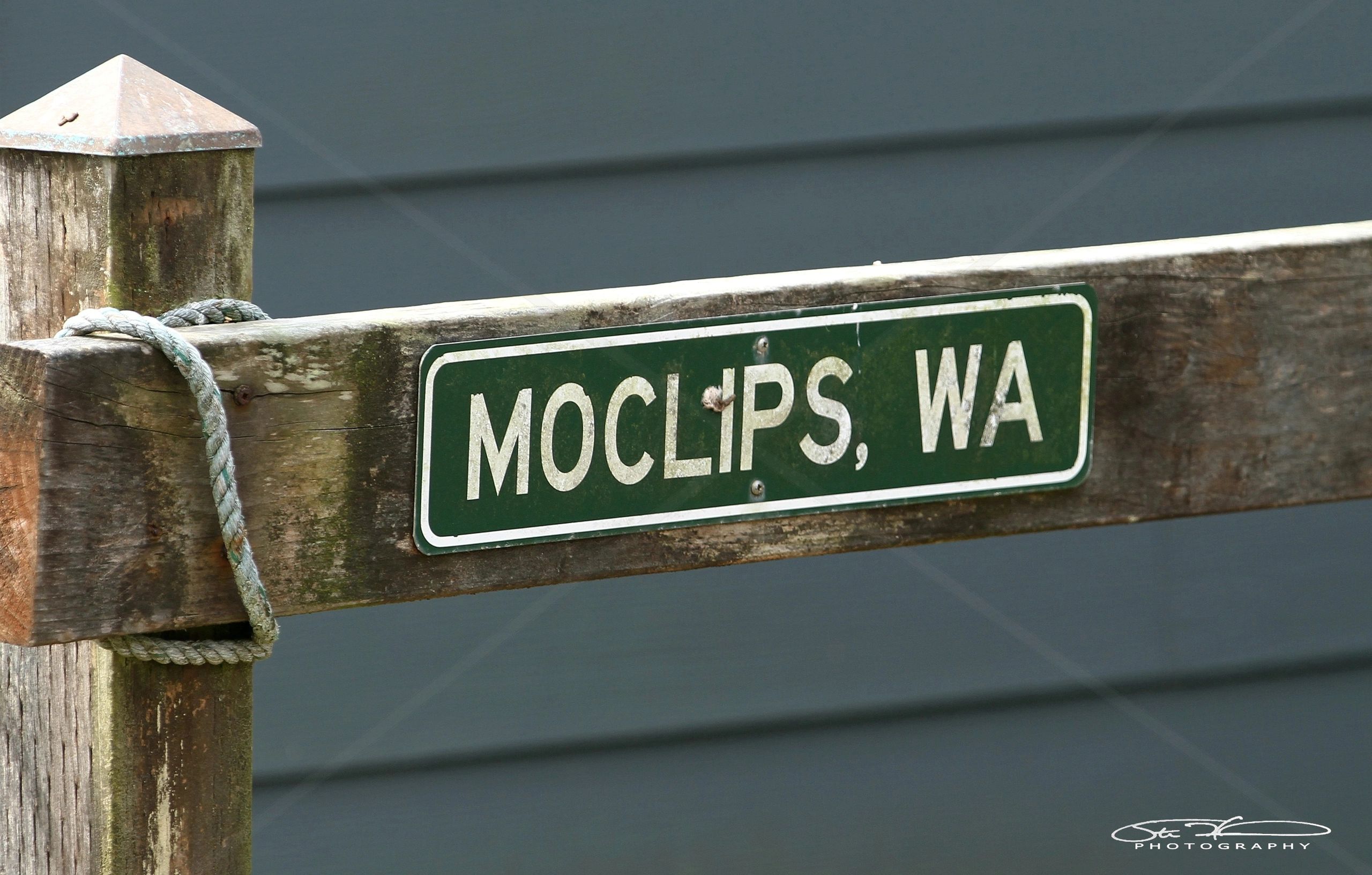 Weathered wooden sign for Moclips, Washington on a post.