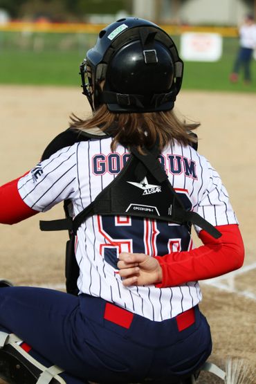 Softball catcher signaling with hand behind back during game.