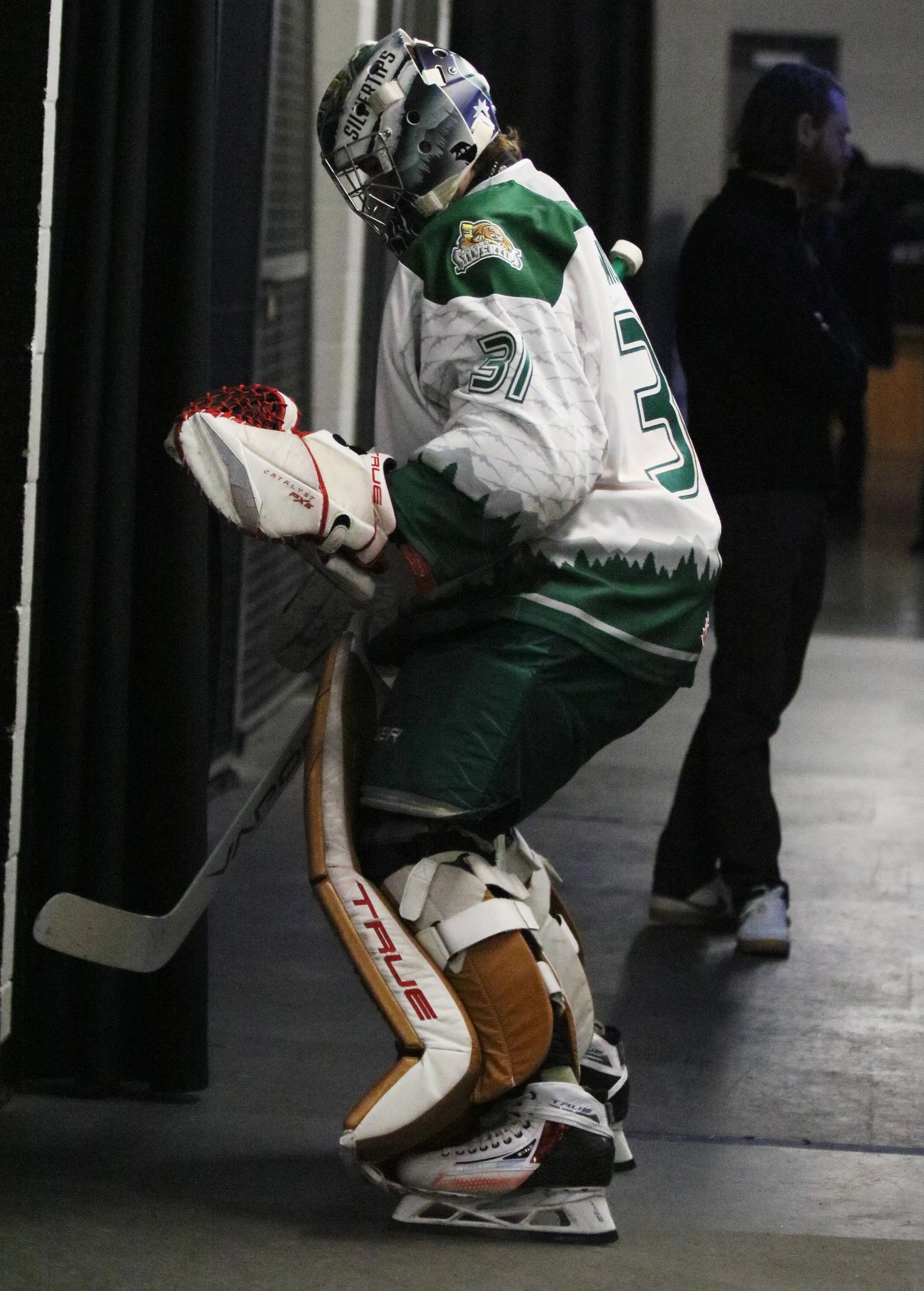 Hockey goalie in full gear leaning against a wall in a corridor.
