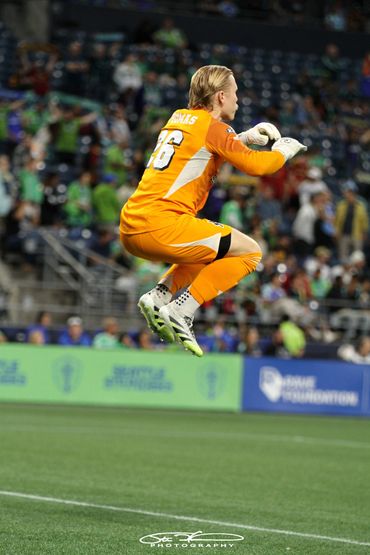 Soccer goalkeeper in orange jersey jumping mid-air during a game.