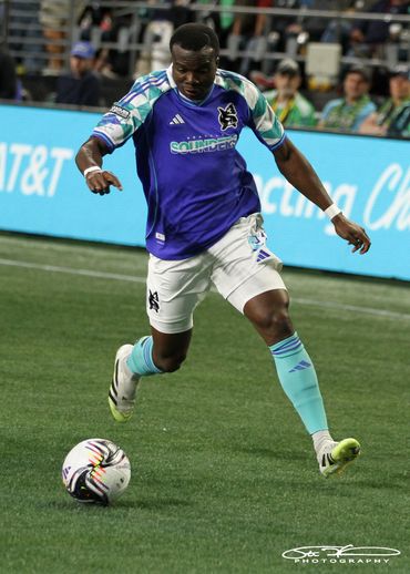 Soccer player in purple and white uniform kicking the ball on the field.