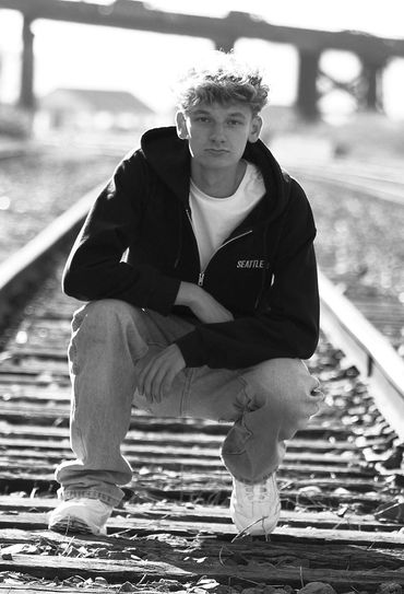 Young man squatting on railroad tracks in black and white photo.