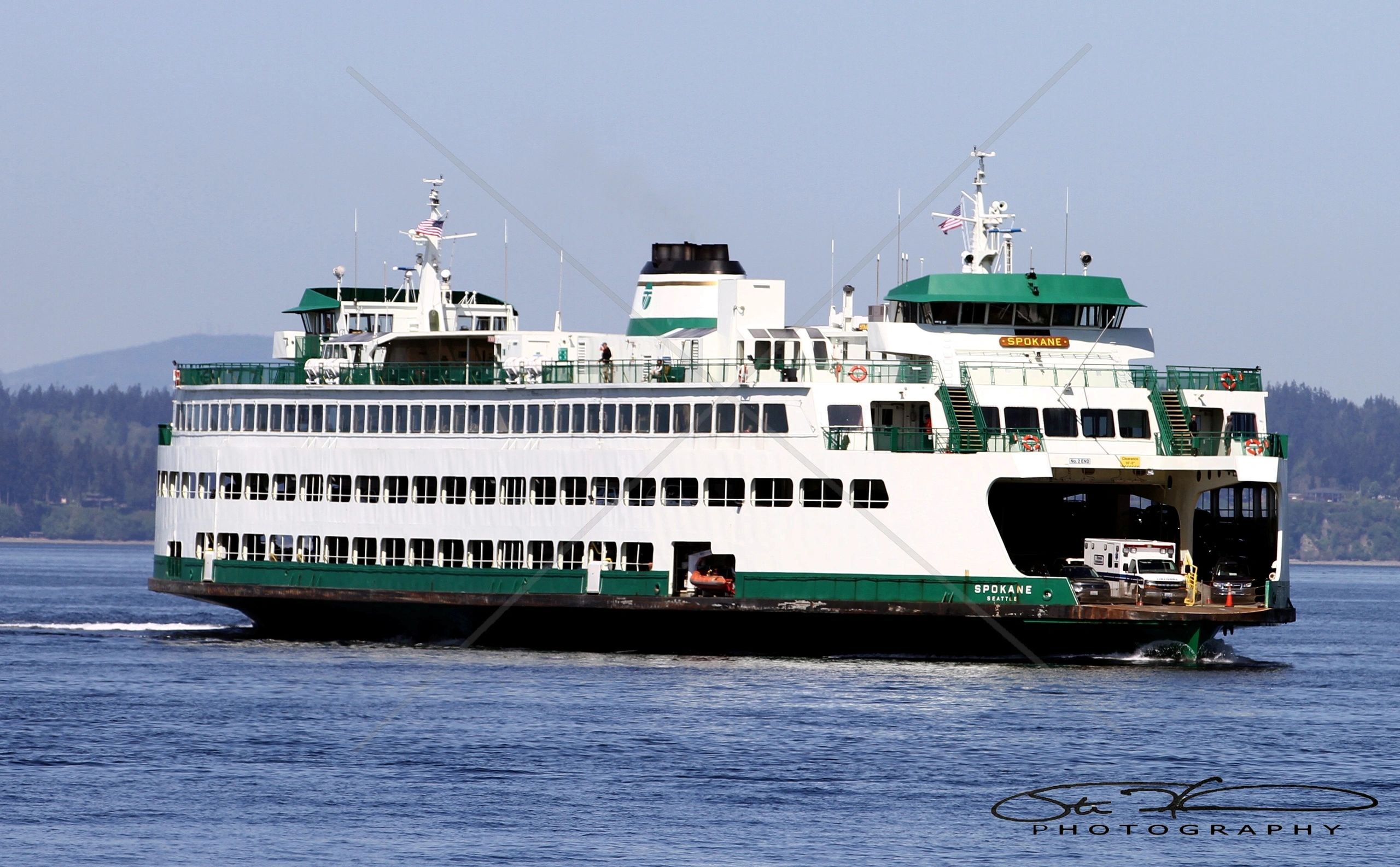 A large white and green ferry named Spokane sailing on calm waters.