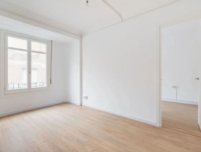 Empty room with wooden floor and white walls, featuring a window and an open door.