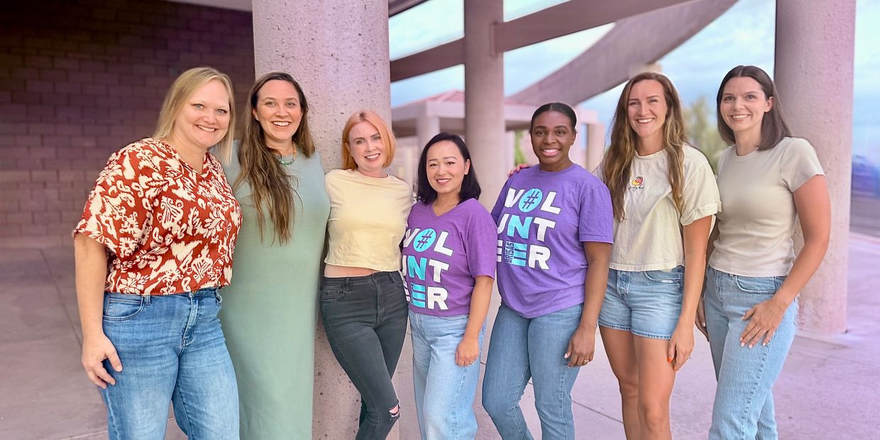 Group of seven smiling women posing outdoors.