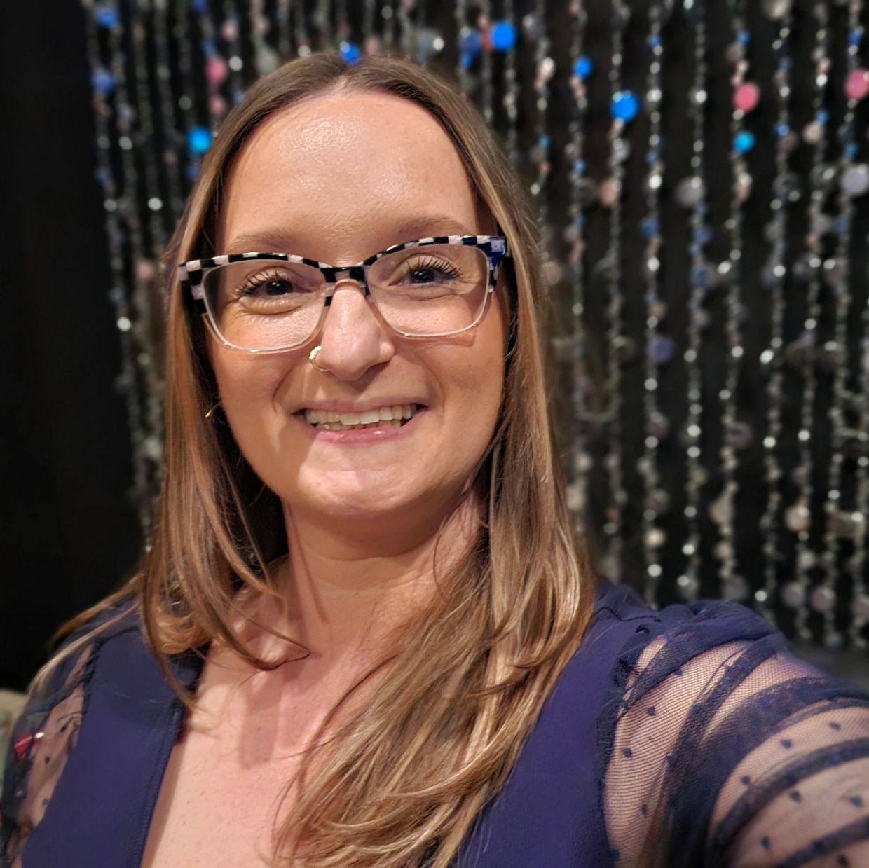 Smiling woman with glasses wearing a navy blue dress with sheer sleeves.