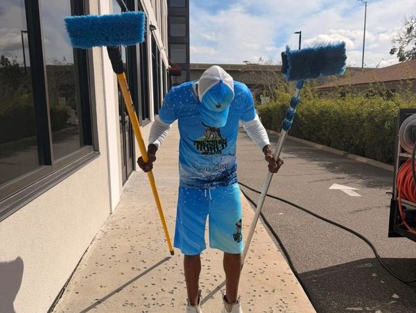 Man holding two large blue cleaning brushes outdoors.