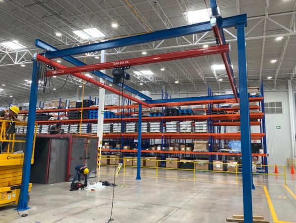 Worker in a warehouse organizing items near shelves and a crane system.