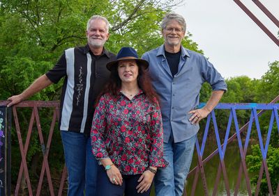 Three people posing outdoors near a fence.