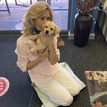 Woman lovingly holds a yellow Labrador puppy indoors.