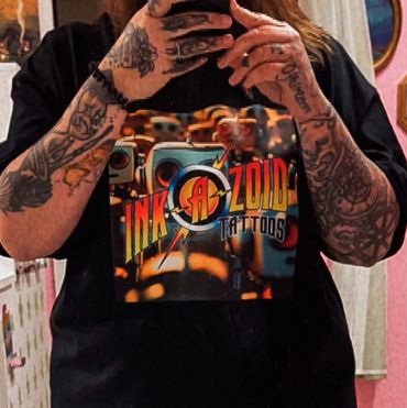 Person wearing an Ink-A-Zoid Tattoos t-shirt with tattooed arms.