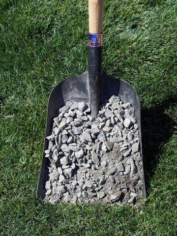 Shovel filled with crushed stones resting on grass.