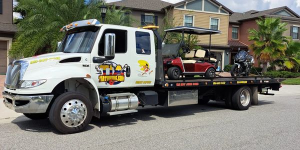 tow truck towing a golf car and a motorcycle