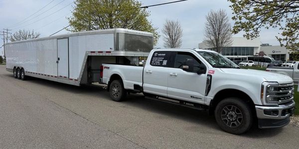 Moving Kingdom white pickup and enclosed trailer prepared for protected vehicle transport.
