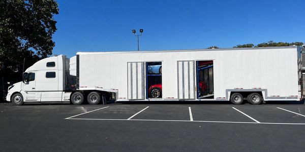 White truck trailer with visible sports cars inside.