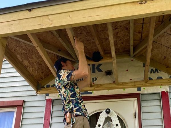 A man on a ladder working on a porch roof under construction.