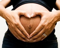 Pregnant belly with hands forming a heart shape.