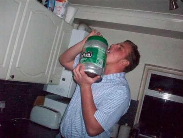 Man drinking from a large Heineken mini keg in a kitchen.