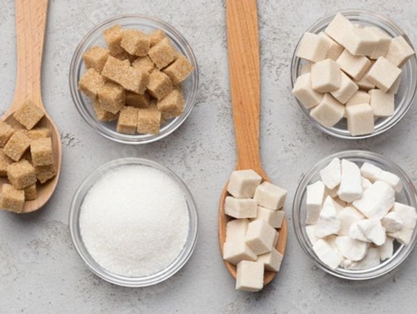 Various types of sugar cubes and granulated sugar in bowls and wooden spoons.