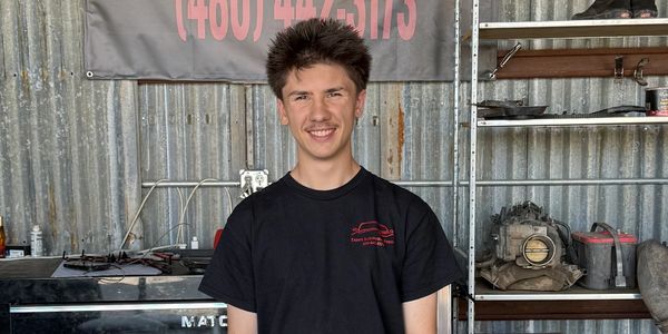 Young man smiling in a workshop with automotive parts in the background.