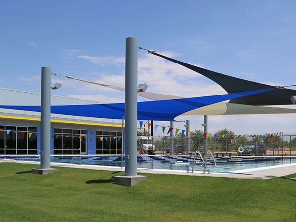 Outdoor swimming pool with shade sails and colorful flags under a clear sky.