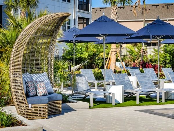 Outdoor poolside seating with woven canopy chair and blue umbrellas.