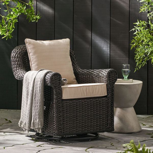 Cozy outdoor wicker chair with cushion and throw blanket beside a modern side table.