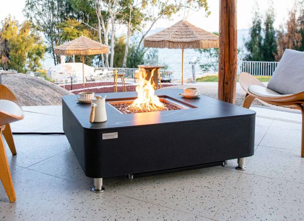 Modern outdoor fire pit table with chairs and parasols in a serene setting.