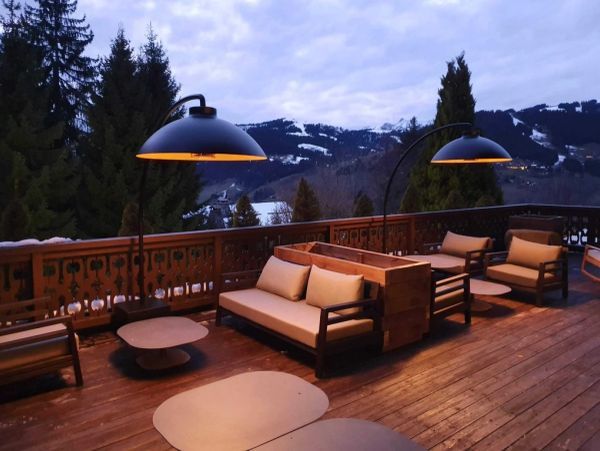 Cozy outdoor seating with warm lighting on a wooden deck overlooking snowy mountains.