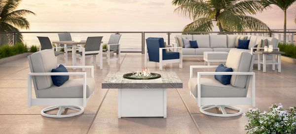Modern outdoor seating area with fire pit and ocean view at sunset.