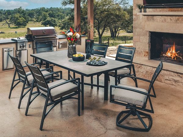 Outdoor dining area with a table, chairs, grill, and fireplace in a scenic setting.