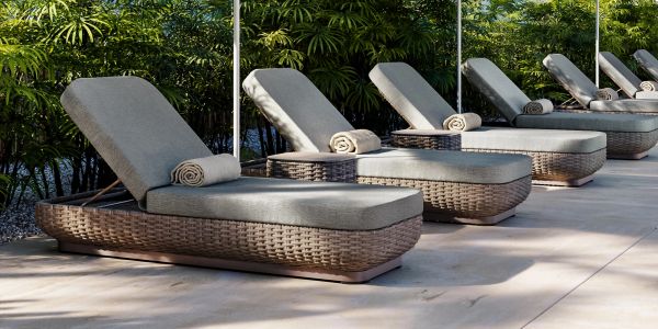 Modern outdoor lounge chairs with rolled towels lined up by greenery.