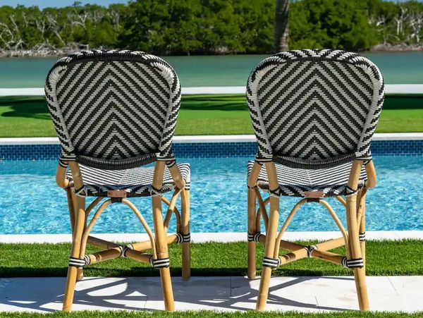 Two patterned chairs by a pool with water and greenery in the background.