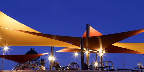 Colorful canopy shades over a nighttime playground with bright lights.