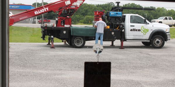 A worker stands by a white utility truck with a crane on a gravel lot.