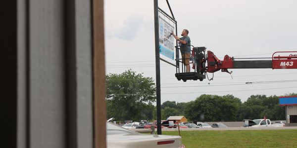 Man working on a billboard using a hydraulic lift on a cloudy day.
