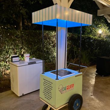 Mobile gelato cart with blue lights and striped canopy at night.