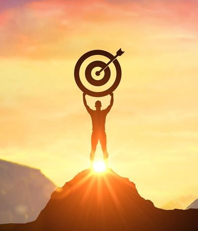 Silhouette of a person holding a target with an arrow at sunset on a mountain peak.