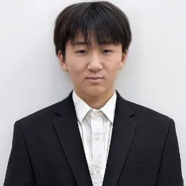 Young man in a black suit and white shirt against a plain background.