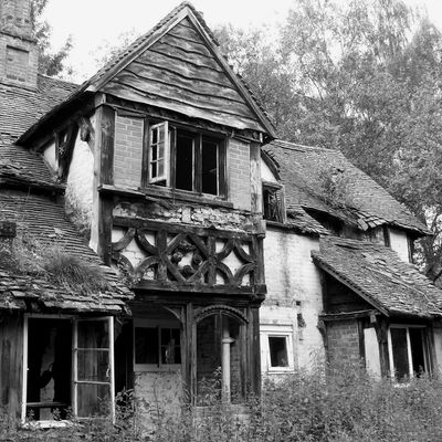 Black and white photo of an old, abandoned, rustic house with broken windows.