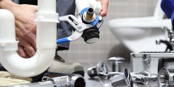 Array of plumbing supplies on the floor while man uses plumbing wrench on pipe